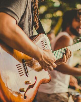 A musician plays a vibrant guitar, focused on their craft, while another performer appears in the background, creating an engaging atmosphere.