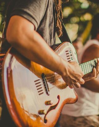 A close-up of a musician's hand playing a beautifully crafted guitar, highlighting intricate details and warm colors in a lively setting.