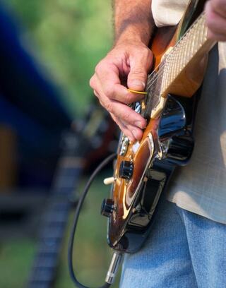 A close-up of a hand skillfully playing an electric guitar, with a blurred background hinting at a lively outdoor music scene.