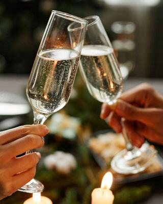Two glasses of sparkling drink clink together, surrounded by a festive table setting, candles, and treats, celebrating a joyful moment.
