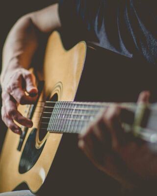 A hand strums an acoustic guitar, highlighting the instrument's rich wood grain and the musician's focus on their craft.