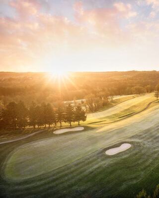 A tranquil golf course bathed in warm sunlight, with lush green rolling hills and sand traps, creating a serene morning landscape.