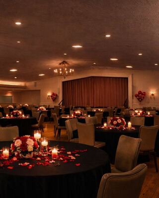 A romantic venue features elegantly decorated tables with red and white flowers, candlelight, and heart accents, creating an intimate atmosphere.