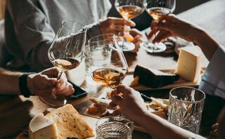 Glasses raised in a toast, surrounded by an elegant spread of gourmet cheeses on wooden boards, creating a warm, celebratory atmosphere.