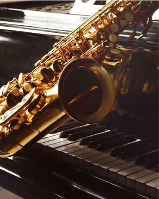 A golden saxophone rests on a piano, creating a beautiful contrast between the shiny instrument and the elegant black keys.