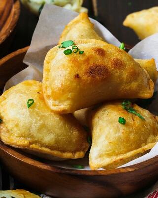 Golden, crispy pastries filled with savory ingredients, garnished with fresh green herbs, nestled in a wooden bowl.