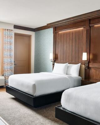 A stylish hotel room features two neatly made beds, warm wooden accents, and soft lighting, creating a cozy and inviting atmosphere.