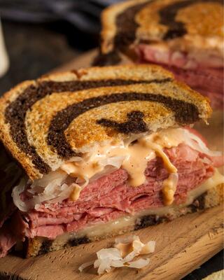 A delicious sandwich layered with corned beef, sauerkraut, and dressing, served on swirled rye bread. Perfectly toasted and inviting.