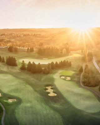 A breathtaking aerial view of a golf course at sunrise, showcasing lush greens, tree-lined fairways, and a tranquil landscape.