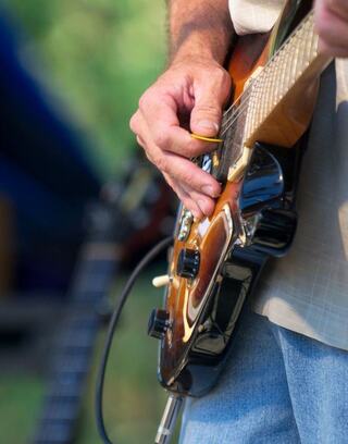 A close-up of a hand skillfully playing a guitar, showcasing its rich finish and details, amidst a vibrant outdoor setting.