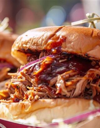 A delicious pulled pork sandwich piled high with tender meat, drizzled in barbecue sauce, and nestled in a soft bun with hints of coleslaw.