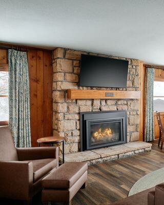 Cozy living room featuring a stone fireplace, a mounted TV, warm wood accents, and plush seating, creating a comfortable atmosphere.