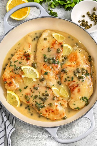 Tender chicken fillets in a creamy lemon sauce, garnished with capers and parsley, accompanied by lemon slices for a fresh touch.