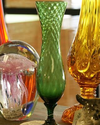 A tall, intricately patterned green glass vase stands among colorful art pieces, showcasing its elegant shape and vibrant hue.