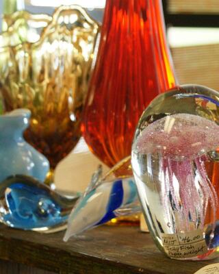 Colorful glass decor items are displayed, featuring various shapes and textures, including a paperweight with a jellyfish design.
