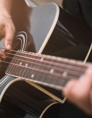 A close-up of hands strumming an acoustic guitar, showcasing intricate details of the strings and body. Warm light adds a soft glow.