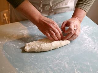 Hands knead and shape dough on a light blue surface, surrounded by a dusting of flour, showcasing the art of bread-making.
