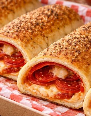 Golden-brown rolls filled with layers of melted cheese and slices of pepperoni, sprinkled with seasoning, resting on red-checkered paper.
