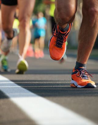Runners in vibrant athletic shoes stride along a racing track, emphasizing motion and energy in a lively outdoor setting.