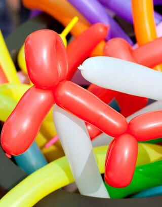 A cluster of colorful balloon animals, prominently featuring a red balloon shaped like a dog, among other vibrant twisty designs.
