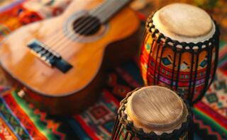 A wooden guitar rests beside colorful drums, all set on a vibrant, patterned textile, evoking a lively musical atmosphere.
