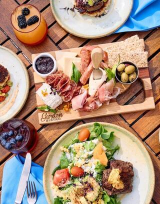 A vibrant spread featuring cured meats, cheese, olives, a fresh salad, and colorful drinks on a rustic wooden table.