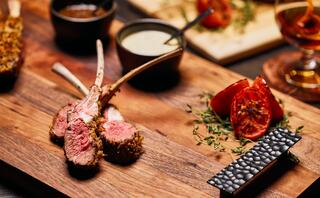 Succulent lamb chops, beautifully plated with roasted tomatoes, herbs, and dipping sauces, create an inviting culinary presentation.