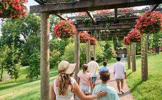 A group of people strolls along a floral-covered pathway, enjoying nature and each other's company on a sunny day.
