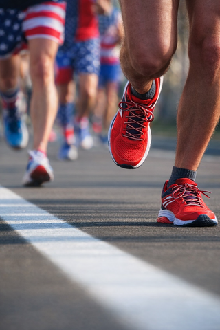 Runners in colorful attire pound the pavement, showcasing vibrant red shoes and patriotic patterns, as they race along a marked line.