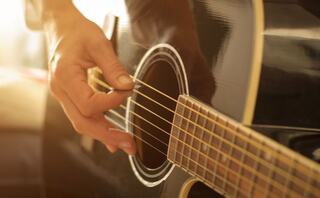 A close-up of a hand playing an acoustic guitar, capturing the strings and body in warm, soft lighting.