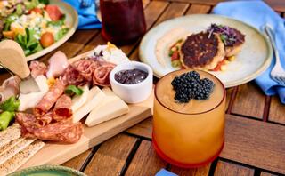 A platter of assorted meats, cheeses, and preserves paired with a vibrant cocktail garnished with blackberries, set on a wooden table.