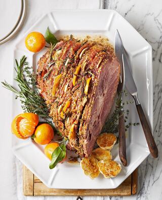 A beautifully presented glazed ham sits on a platter, garnished with fresh herbs and citrus fruits, showcasing a festive, appetizing arrangement.
