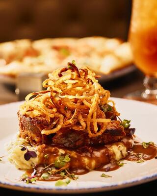 A hearty dish features tender meat atop creamy mashed potatoes, smothered in gravy and topped with crispy fried onions.