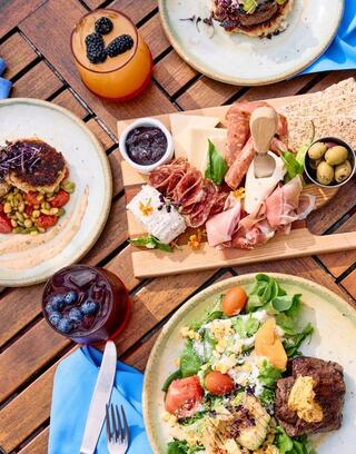 A vibrant spread of gourmet dishes, including salads, charcuterie, and drinks, beautifully arranged on a wooden table.