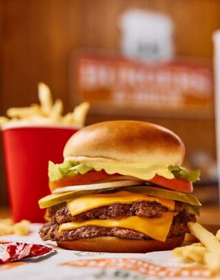 A juicy burger with cheese, lettuce, tomato, and pickles sits beside crispy fries in a red container, showcasing a tasty meal.