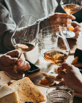 Cheers with glasses of amber drink and a variety of cheeses and snacks, creating a warm, social atmosphere among friends.
