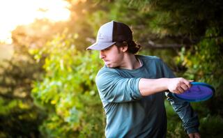 A young man in a cap throws a blue disc against Oglebay's backdrop of lush greenery, illuminated by warm sunlight.