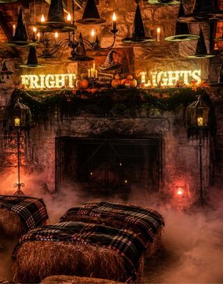 A spooky setting features hay bales draped in plaid, a stone fireplace, and décor like hanging witch hats, pumpkins, and eerie lighting at Schenk Lake boathouse.