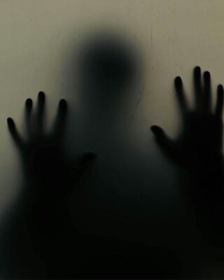 A shadowy figure presses against a translucent surface, hands outstretched, evoking a sense of entrapment or longing.