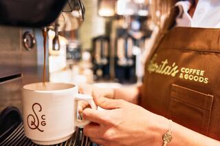 A barista in an apron pours coffee into a branded mug, showcasing the brewing process in a cozy café setting.