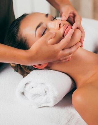 A woman receives a soothing facial treatment, with gentle hands massaging her face, highlighting relaxation and skincare. Towels provide comfort.
