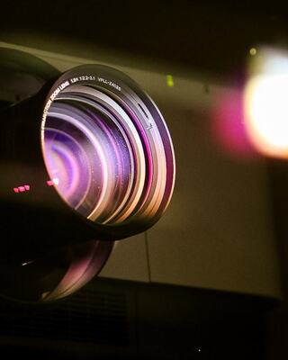 A close-up view of a camera lens, showcasing vivid reflections and colors, with hints of light flares in the background.