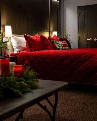 Santa Suites at Oglebay features a red quilted bedspread with decorative pillows, soft lighting, and a festive touch with greenery and candles.