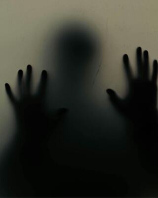 A shadowy figure presses against a translucent surface, hands outstretched, creating an eerie and haunting atmosphere.