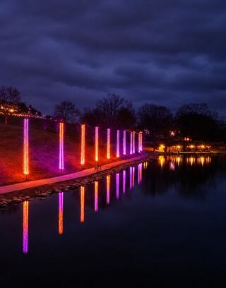 Colorful vertical lights reflect on Schenk Lake under a moody, overcast sky, creating a spooky and enchanting atmosphere.