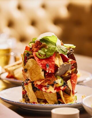 A towering stack of colorful nachos topped with herbs, cheese, and jalapeños, served on a plate with a side of dipping sauces - tin can nachos at Oglebay's Skyline Kitchen & Bar.