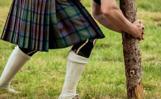 A person in a kilt grips a log during a strongman competition, showcasing determination and athleticism on a grassy field.