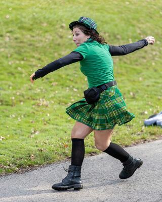 A person in a green outfit and plaid skirt playfully turns while walking along a path, showcasing spirited energy and fun.