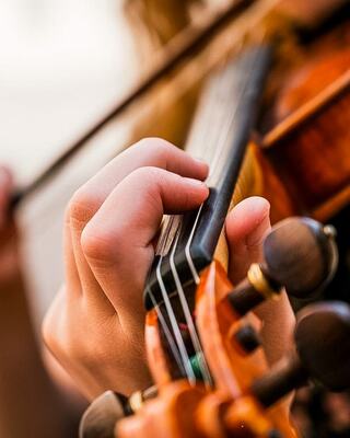 A close-up of a hand expertly pressing the strings of a violin, showcasing the intricate details of the instrument and the player's focus.