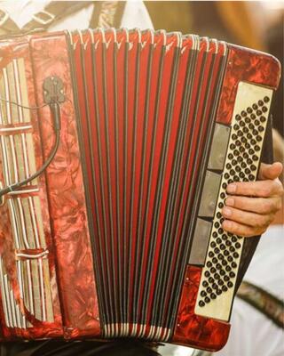A close-up of a vibrant red accordion, showcasing its keys and bellows, held by a musician in a festive setting.